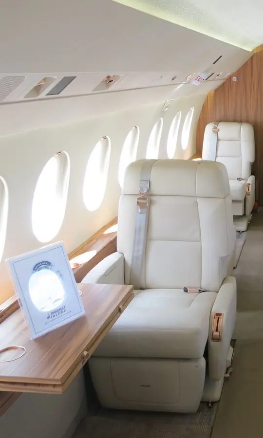 Kabine eines Falcon 2000LX, Blick nach hinten: cremefarbene Clubsessel aus Leder, ein ausklappbarer Tisch und ovale Fenster