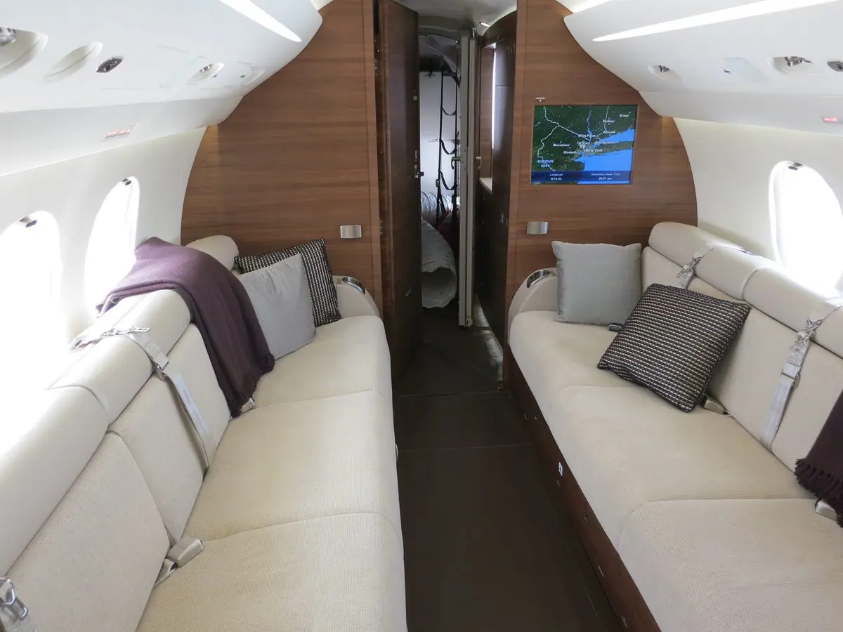 Lounge im Heck eines Falcon 7X mit zwei gegenüberliegenden Sofas und einem Bildschirm mit Moving Map