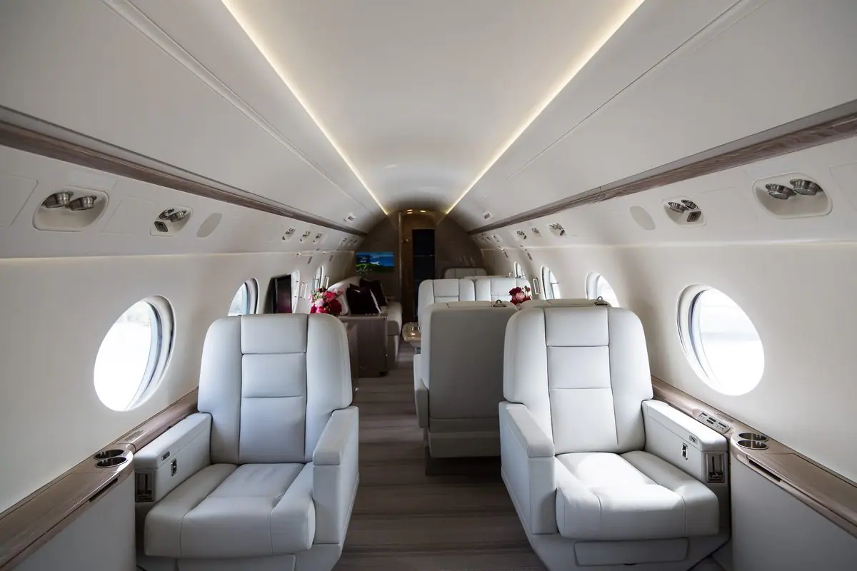 Kabine eines Gulfstream G550, Blick nach hinten an cremefarbenen Clubsesseln aus Leder und ovalen Fenstern vorbei